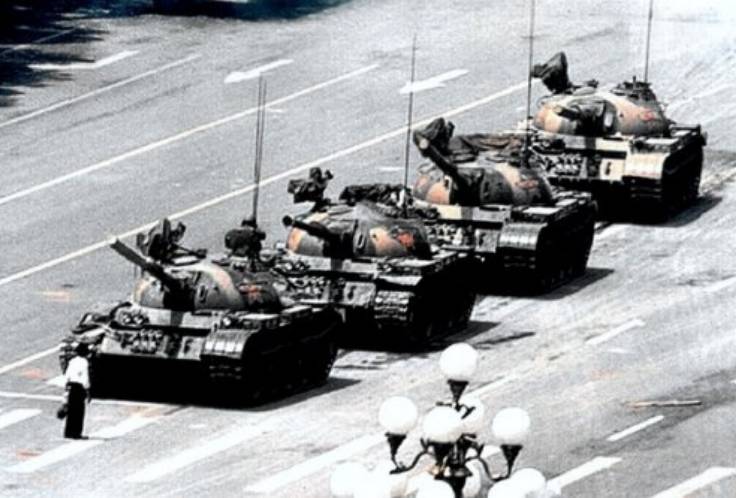 Bu görsel, üst açıdan kamera ile çekilmiş, siyah beyaz bir fotoğraf. Fotoğrafta, geniş bir yolun orta kısmında arka arkaya 4 adet tank bulunuyor. En öndeki tankın hemen önünde ise bir insan bulunuyor. Fotoğraf Çİn' de, 1989 yılında Tiananmen Meydan Protestolarında çekilmiş. Jeff Widener tarafından çekilmiş bu fotoğraf, dört tankı tek başına durdurmaya çalışan bir protestocuyu göstermektedir. Bu fotoğraf, 20. yüzyılın en ünlü fotoğraflarından biri haline gelmiş ve Soğuk Savaş döneminin sonunun uluslararası simgelerinden biri olmuştur.