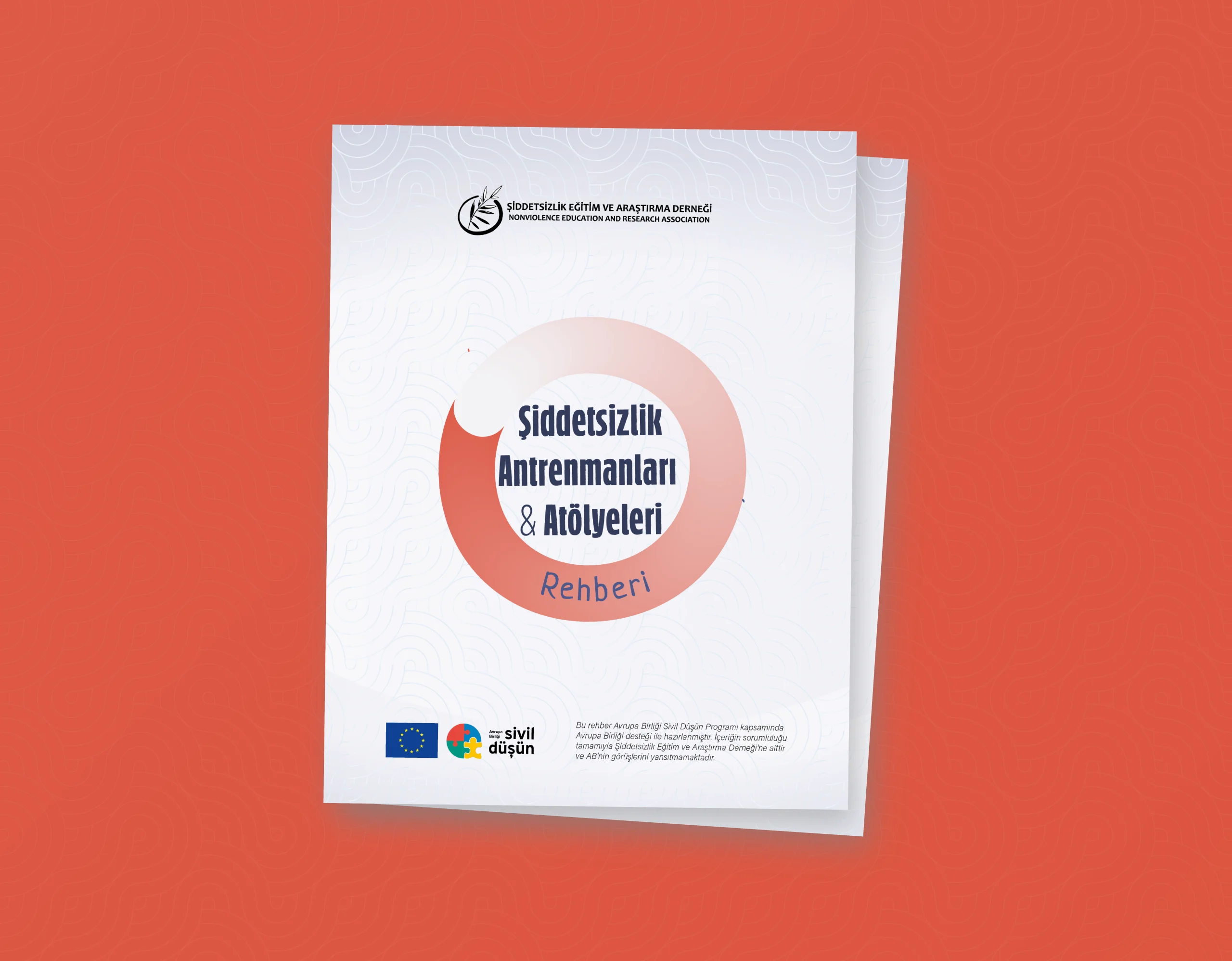 Görselde, Şiddetsizlik Eğitim ve Araştırma Derneği tarafından hazırlanan bir rehberin kapak tasarımı yer alıyor. Rehberin adı büyük harflerle, merkeze yerleştirilmiş dairesel bir grafik içinde yazıyor: “Şiddetsizlik Antrenmanları & Atölyeleri Rehberi”. Daire, kırmızımsı bir tonla başlayıp açık pembeye doğru yumuşayan bir geçişle tasarlanmış. “Rehberi” kelimesi dairenin alt kısmına eğrisel biçimde eklenmiş ve mavi renkte yazılmış. Üst kısımda Şiddetsizlik Eğitim ve Araştırma Derneği logosu ve ismi, hem Türkçe hem İngilizce (Nonviolence Education and Research Association) olarak yer almakta. Alt kısımda ise Avrupa Birliği ve Sivil Düşün logoları bulunuyor. Bu logoların hemen yanında rehberin Sivil Düşün Programı kapsamında hazırlandığını belirten küçük puntolu bir açıklama yer alıyor. Arka plan, beyaz üzerine ince çizgilerle yapılmış, soyut dalga desenleriyle sade ama dinamik bir görünüm sunuyor. Tüm bu tasarım, kırmızı tonlarında bir zemin üzerine yerleştirilmiş ve rehber kapağı hafif sağa doğru açılı şekilde gösterilerek üç boyutlu bir etki yaratılmış.